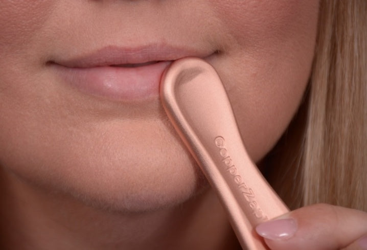 Close-up of a person using a copper tool on their lips.